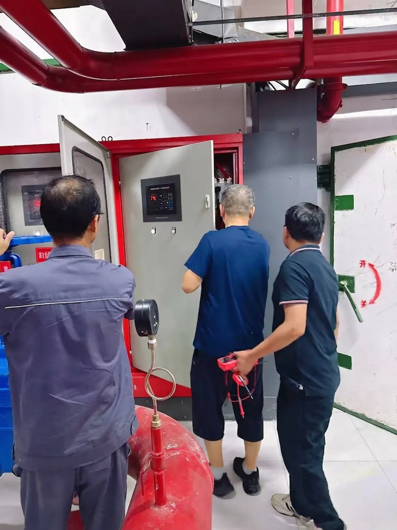 橘舍青年酒店合肥高新区汽车西站地铁站店开业前消防验收现场：验收人员检查消防联动控制柜与喷淋管路